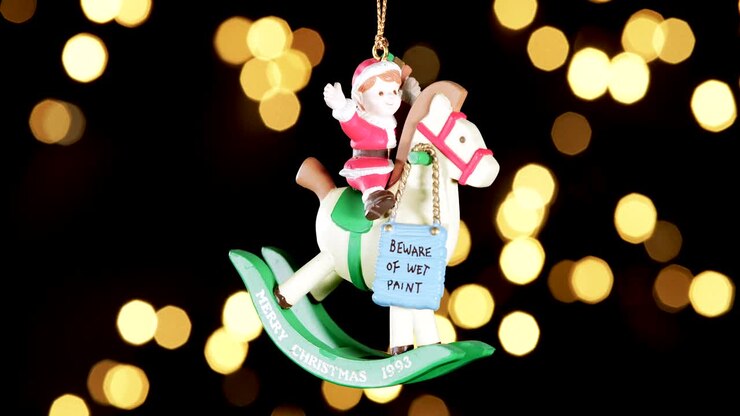 single wooden Christmas ornament of a boy on a rocking horse with out of focus lights flickering in the background, close up