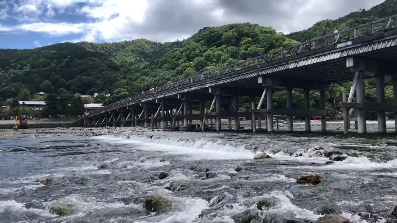 Ghi lại toàn cảnh yên bình từ phía hạ lưu Cầu Togetsukyo ở Kyoto, lia máy dần sang trái để lộ toàn bộ cây cầu. Trải nghiệm cây cầu biểu tượng dưới bầu trời trong xanh, nắng đẹp.