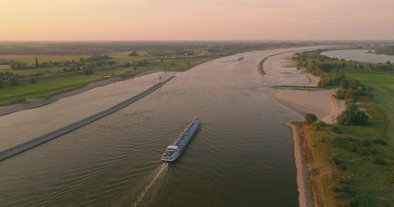 Splendida ripresa con drone di una nave da carico che naviga attraverso un canale olandese al tramonto, circondata dall'iconico paesaggio dei polder e da cieli vivaci e colorati sulla tranquilla campagna