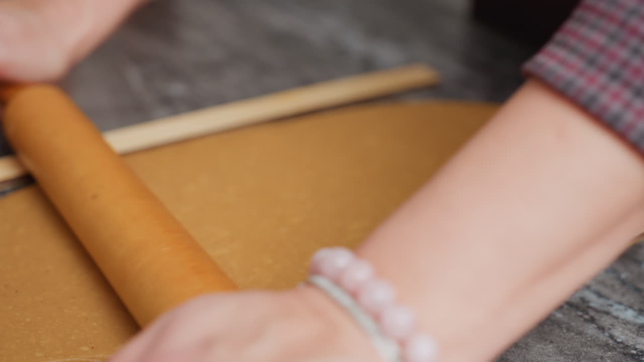 primer plano de las manos de la mujer rodando masa marrón con rodillo de madera, mano izquierda adornada con un brazalete, ligero borrón en el fondo añadiendo profundidad