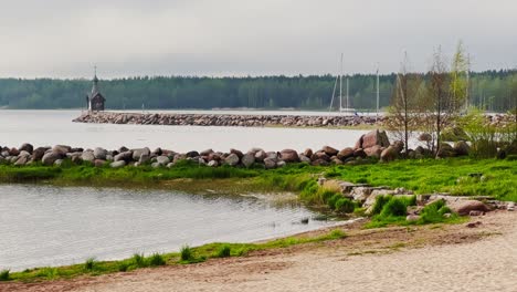 an old chapel stands on a stone promontory on the water in leningrad region russia at cloudy weather, the forest in the background