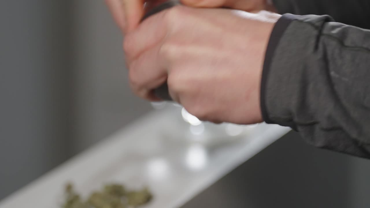 Hand puts dried plant nuggets into grinder