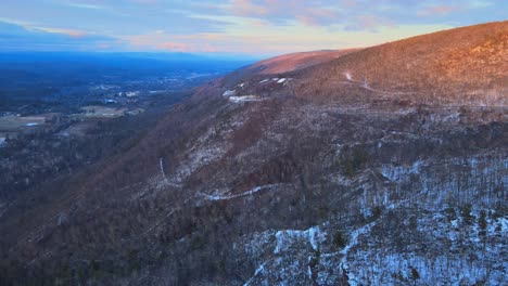 Aerial-footage-of-a-forested-mountain-valley-with-a-light-coating-of-snow-during-winter-in-the-Appalachian-Mountains-during-sunset’s-golden-hour-in-winter