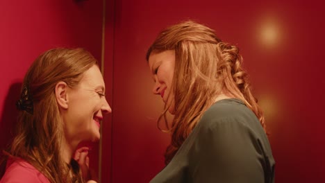 close pan to a woman seductively whispering in the ear of another woman. they smile and walk away