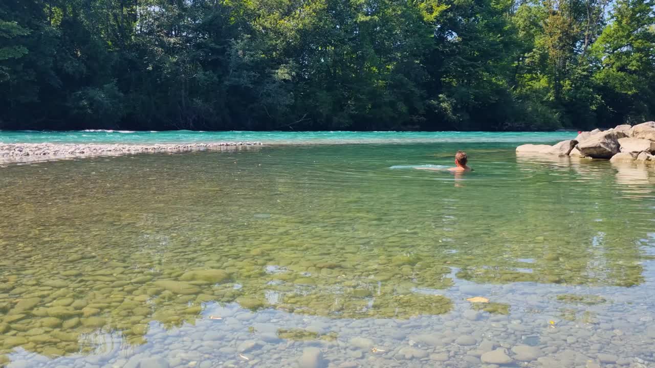 Man enjoying a summer swim in the crystal-clear turquoise waters of the Aare River, relaxing in the midst of lush nature and refreshing scenery