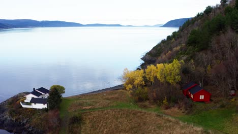 tranquil waters of fjord with rural houses and forest with autumn colors in norway