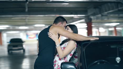 Una-Pareja-Joven-En-Movimiento-Redondo-Se-Abraza-Apasionadamente-Cerca-De-Un-Auto-Negro