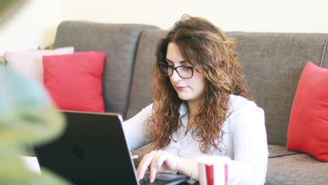 mujer joven que trabaja en línea desde casa escribiendo en una computadora portátil, enfocada en su deber después de las medidas de bloqueo del brote de coronavirus