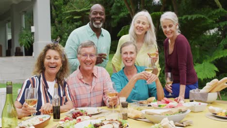 animation of diverse happy senior female and male friends eating lunch in garden