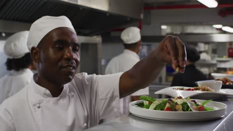 chef afroamericano de sexo masculino adornando platos y simulando en la cocina del restaurante