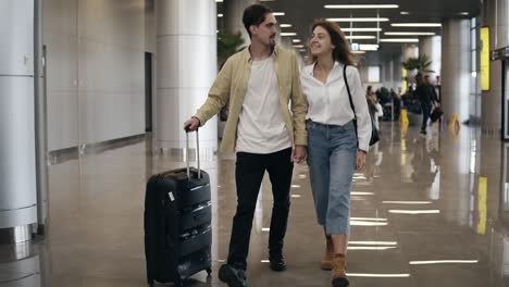 Front-view-of-smiling-couple-walking-together-in-airport-going-on-vacation-or-trip.-Travel-together.-Attractive-caucasian-young