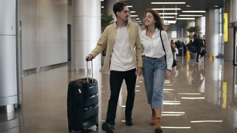 vista frontal de una pareja sonriente caminando juntos en el aeropuerto yendo de vacaciones o viaje. viajar juntos. joven caucásico atractivo