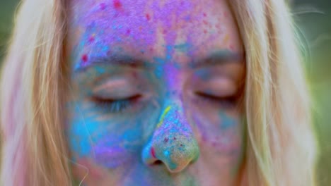 close up of the face of the young blond beautiful woman with colorful paints on her face looking straight to the camera and smiling