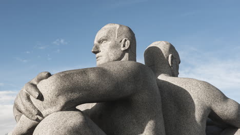 granite sculpture of two men sitting back to back with crossed arms at vigeland installation in frognerparken, oslo, norway