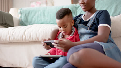 african american sister and brother using tablet and smartphone in living room, slow motion