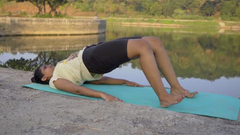 chica amateur haciendo pose de yoga pose de puente setu bandha sarvangasana junto al lago