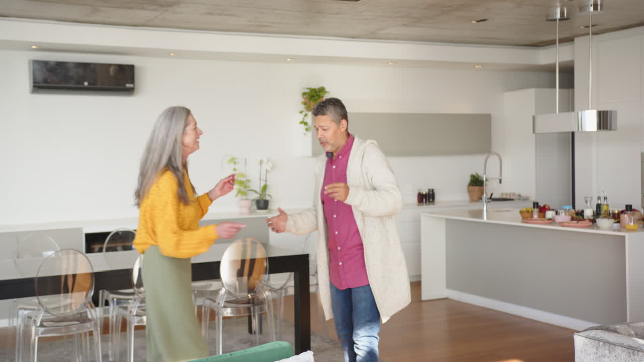 Dancing together, multiracial senior couple enjoying intimate moment in modern home kitchen