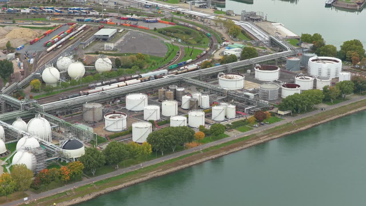 石油貯蔵タンク、石油精製所、川沿いを通過する貨物列車がある広大な工業団地の上空を飛ぶ空撮