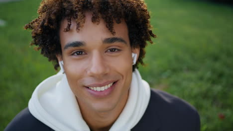 Happy-guy-using-earphones-green-grass-portrait.-Earbuds-student-smiling-toothy