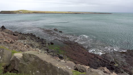 Tracking-shot-of-waves-splashing-on-the-rocks-on-a-cloudy-day-in-Scotland,-isle-of-Skye