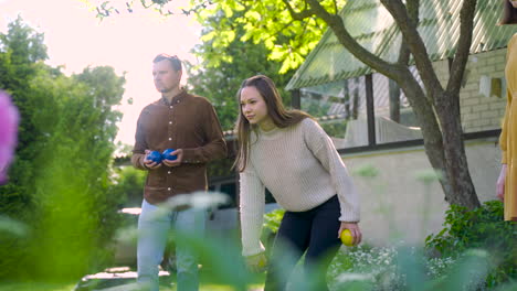 caucasian young woman throwing a yellow petanque ball in the park on a sunny day while her friends wait their turns