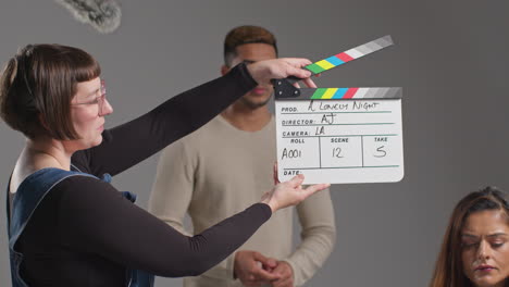 Female-Assistant-On-Film-Set-In-Studio-Using-Clapperboard-Or-Slate-On-Movie-Or-Video-As-Actors-Start-Scene-3