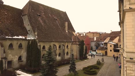 a drone shot,with pedestal upward motion, capturing a glimpse a closed locality in the city of sighisoara on an afternoon, with residual snow on the roof of and outside apartments