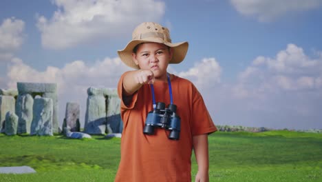 asian boy with a hat and binoculars pointing his finger towards you and furiously speaking against blaming you while traveling in stonehenge. boy researcher, travel tourism adventure concept
