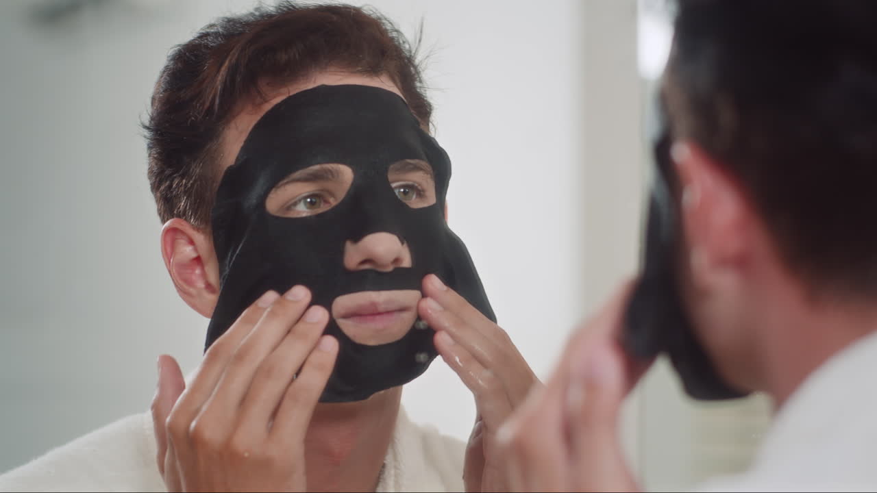 Male Zoomer Applying Charcoal Mask on Face in front of Mirror