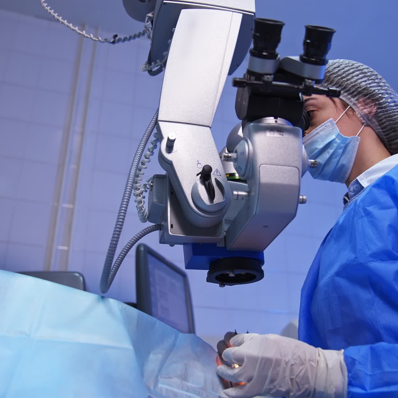 Ophthalmological surgery specialist sits in front of microscope performing operation. Low angle view on the female doctor conducting high-precise surgery