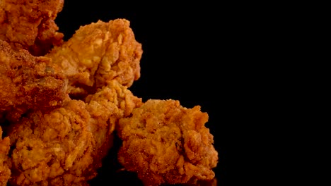 golden, crispy fried chicken pieces rotate and zoom in slow motion against a black background, highlighting texture, spices, and oily sheen under studio lighting