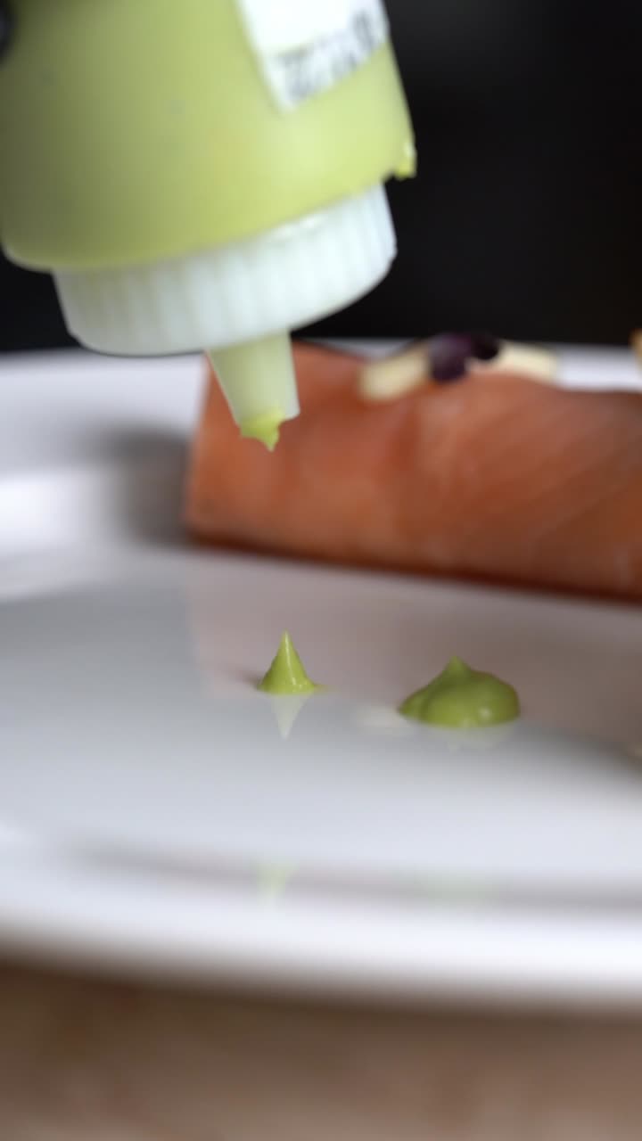 Billede af grøn sauce, der sprøjtes ud i små prikker på en blank hvid overflade i et professionelt køkken, nærbillede