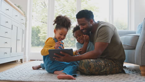 Armeevater-In-Uniform-Zu-Hause-Auf-Urlaub-Mit-Kindern,-Die-Auf-Einem-Teppich-Sitzen-Und-Ein-Digitales-Tablet-Benutzen