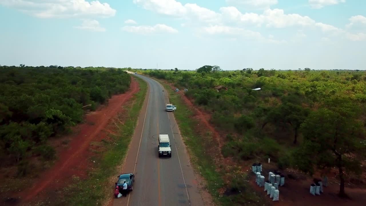 A Utility Vehicle With Tourists Entering Small Town In Kenya, East Africa. - Drone Backward Shot