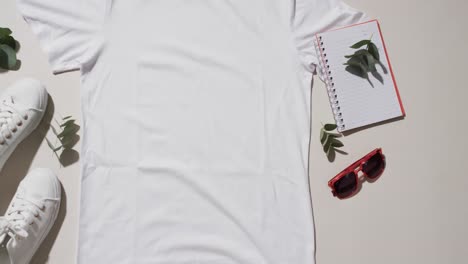 Video-of-flat-lay-of-white-t-shirt,-sneakers,-sunglasses-and-copy-space-on-white-background