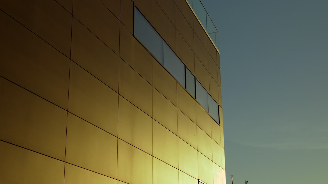 Golden sunlight bathing a modern building's glass facade with blinds and city reflections