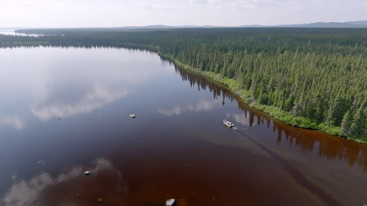 amplia toma aérea captura barco trolling a lo largo de las orillas de un hermoso lago canadiense