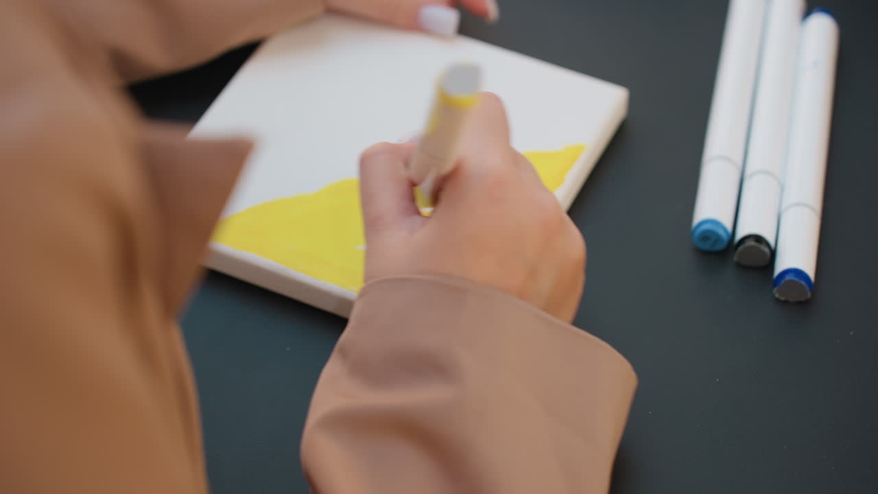 대담한 컬러 스케치, 손과 마커의 클로즈업, 백인 일러스트레이터가 마커로 생생한 컬러 블록을 만들고, 작은 캔버스에는 대담한 색상의 인상적인 마커 스트로크와 손의 클로즈업이 담겨 있어요.