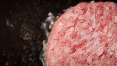 raw beef burger is fried in a frying pan.