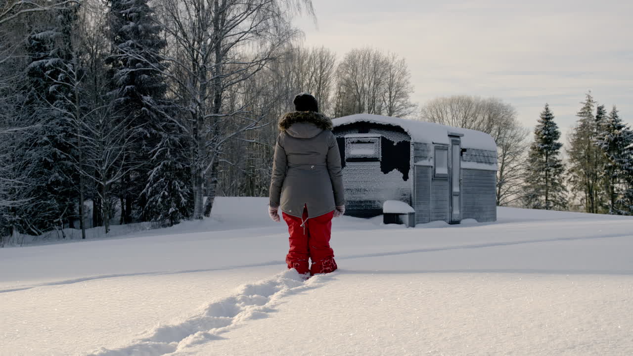 de un tiro de una mujer pasos en la nieve alta hacia una pequeña cabaña de madera en un frío día de invierno