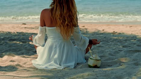 woman meditating on the beach with a coconut