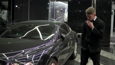 Portrait-of-a-young-man-in-a-black-suit-with-a-bow-tie-smoking-a-cigarette-by-the-black-luxury-car-at-night.