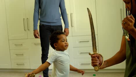 vista lateral de una joven madre negra y su hijo jugando con una espada de juguete en un cómodo hogar 4k
