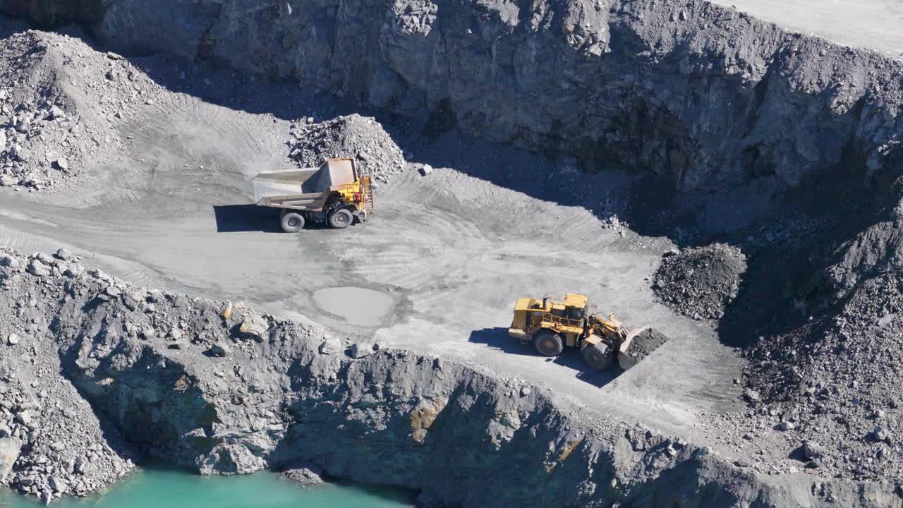 Drone footage captures excavators and trucks in a bustling quarry, highlighting industrial activity under bright daylight