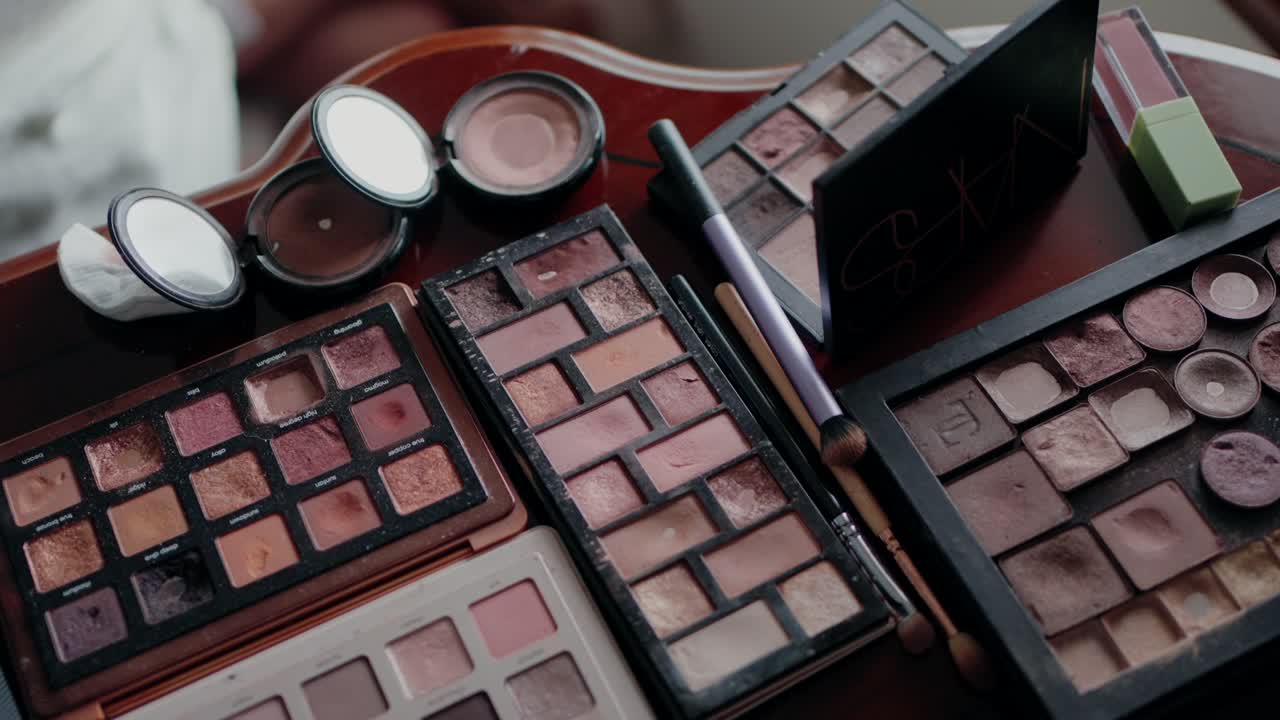 Close up of used eyeshadow palettes and makeup brushes on a wooden table
