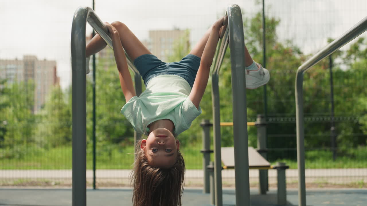Young girl with curly hair having fun outdoors. Multiracial girl delights while swinging over park equipment. Playful young girl with curly hair focuses on swinging above urban park bars