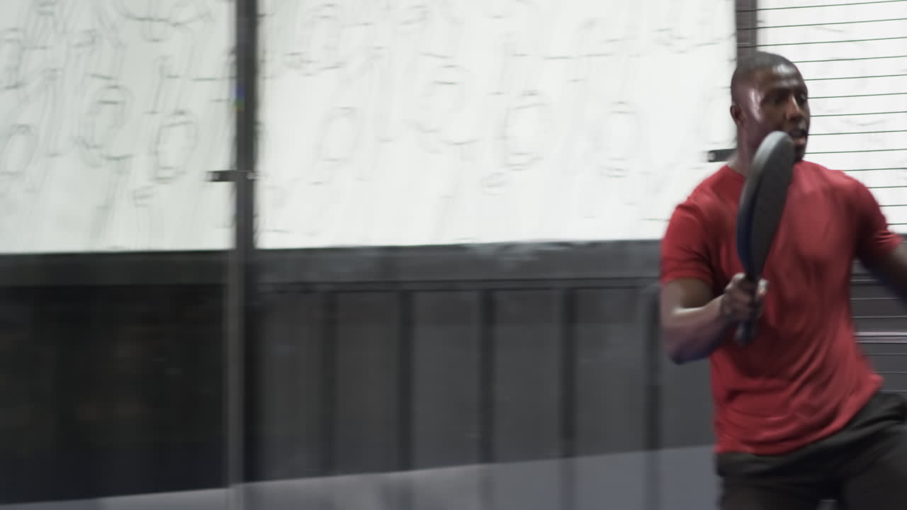 African American man picking up padel racket on indoor court, preparing for match