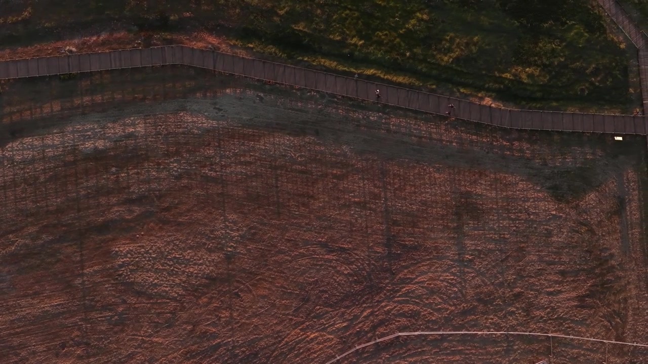 Drone shot of people walking on a wood path at sunset with big shadows.