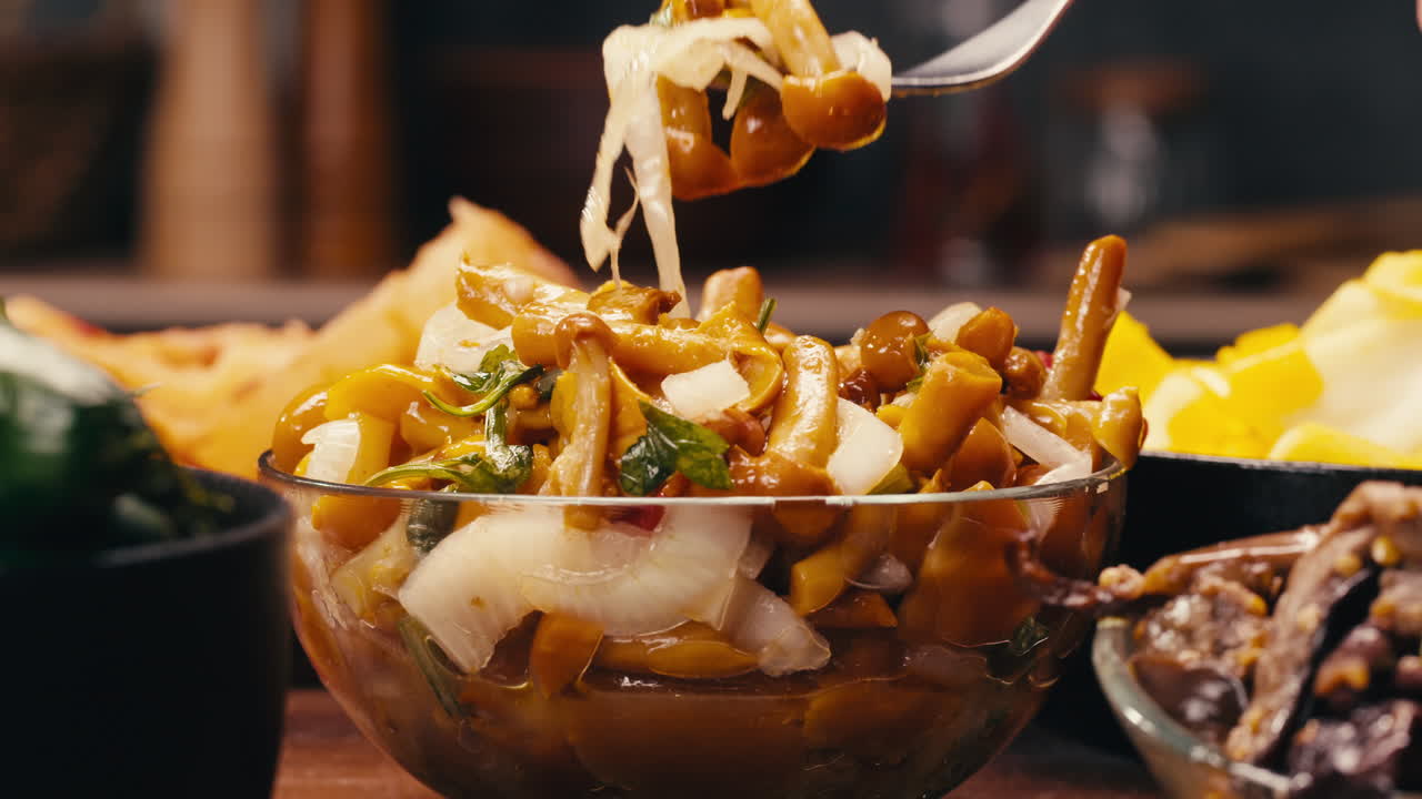 Taking a little bit of fermented yellow honeydew mushrooms with onion by fork close-up. Preservation of vegetables in glass jars. Fermentation preserved mushroom with spices. Asian cuisine.