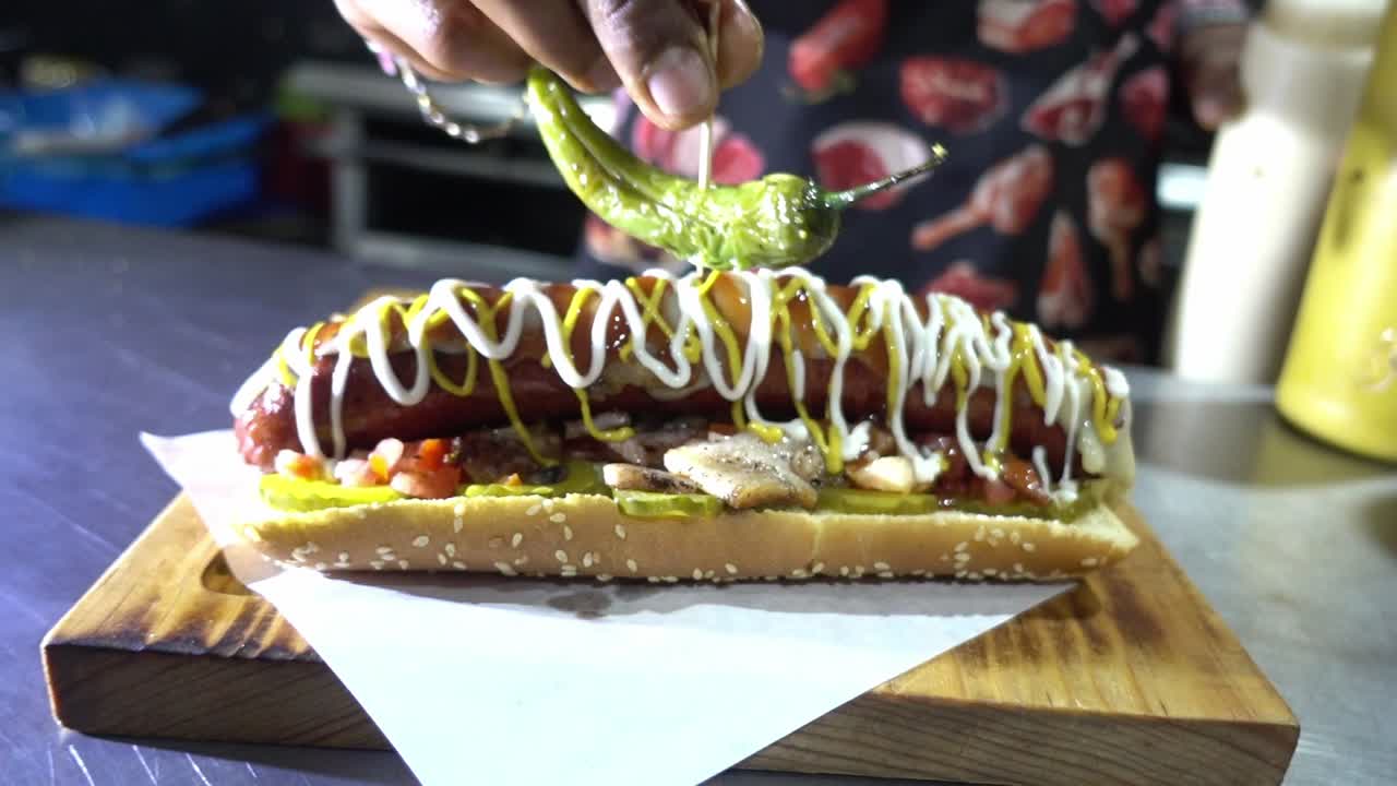 Tomada em câmera lenta de um chef adicionando um jalapeño para finalizar o cachorro-quente em um restaurante